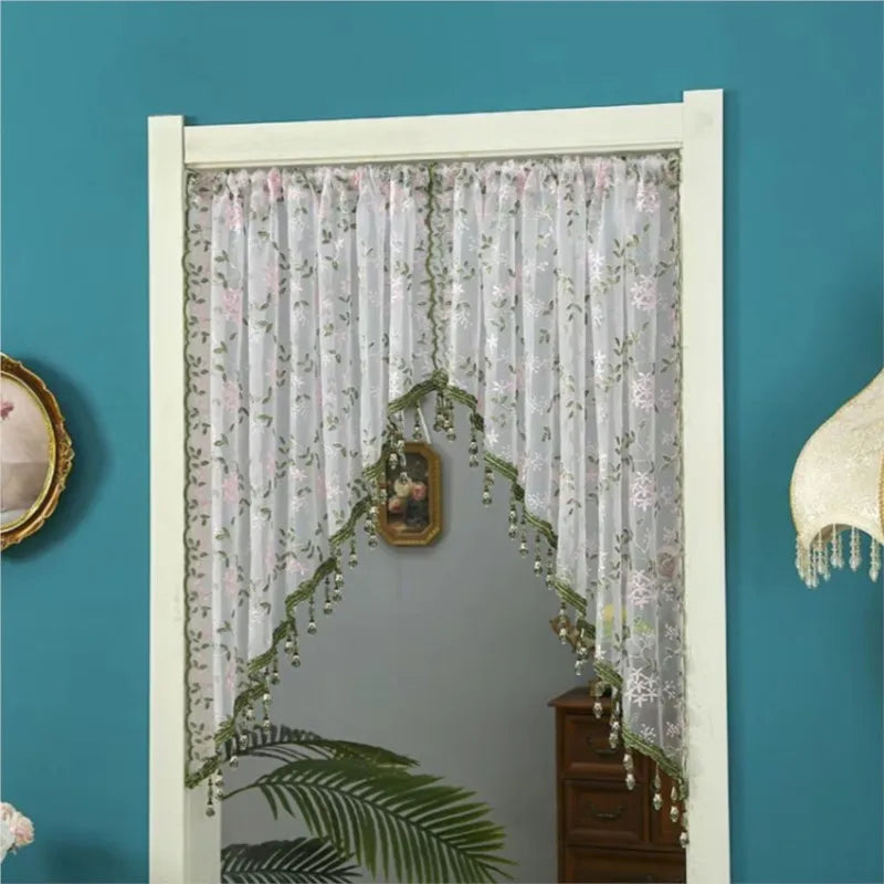 A sheer lace door curtain with pink floral accents hangs in a white frame against a teal wall.