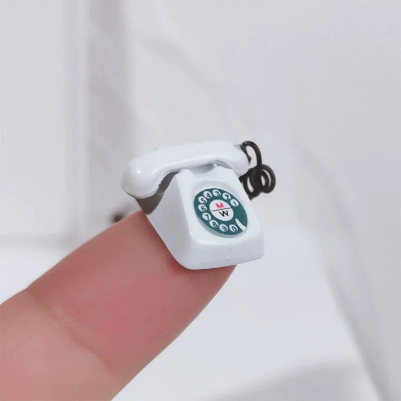 A white vintage rotary desk phone miniature decor is held by a finger against a white background.