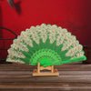 An elegant folding fan with a green silk and gold embroidered design displayed on a wooden stand.