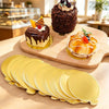 Un plateau en bois présente des gâteaux décorés sur des plateaux dorés et une pile de plats à dessert jaunes réutilisables.
