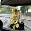 Hand-knitted hanging plant basket with green leaves and white flowers hanging from a car mirror.