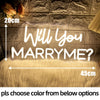 A neon sign asking Will You Marry? is displayed on a textured wall with a fluffy golden surface.