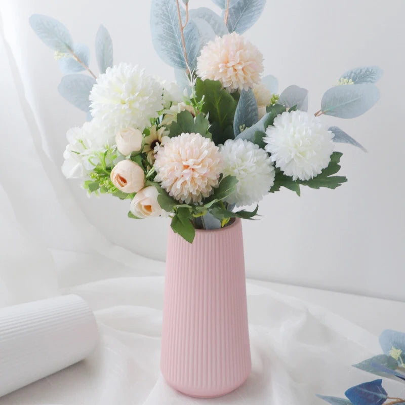 A pink vase holds a bouquet of white and blush flowers with dusty blue eucalyptus leaves.