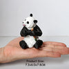 A realistic panda figurine with black and white fur is held in a person's hand.