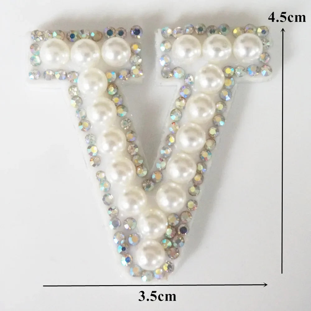 A white alphabet letter T made of pearls and rhinestones on a square patch.