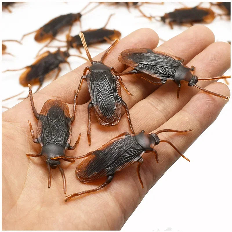 A hand holds several realistic plastic bugs including cockroaches, centipedes, and scorpions.