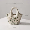 A white ceramic milk pitcher with a handle and pastoral floral design, shown against a light background.