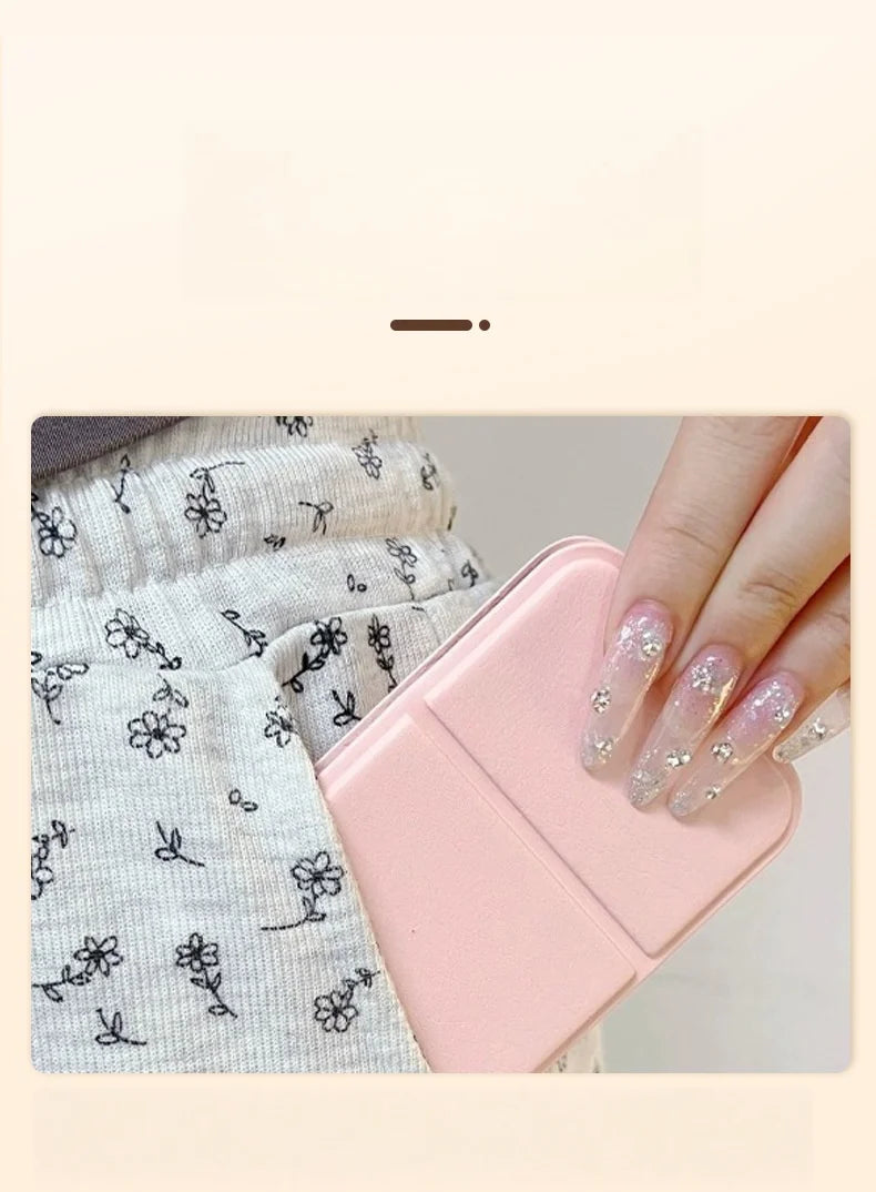 A hand holds a pink portable folding HD makeup mirror with a glitter finish against a light gray patterned fabric.