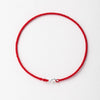 A handmade red string bracelet with a gold plated clasp laid flat on a white background.