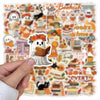 A hand holds a sheet of Bookish Autumn Graffiti stickers featuring cute ghost and book designs.