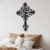 Black decorative metal cross wall art featuring a detailed rose design mounted on a white wall above bedding.