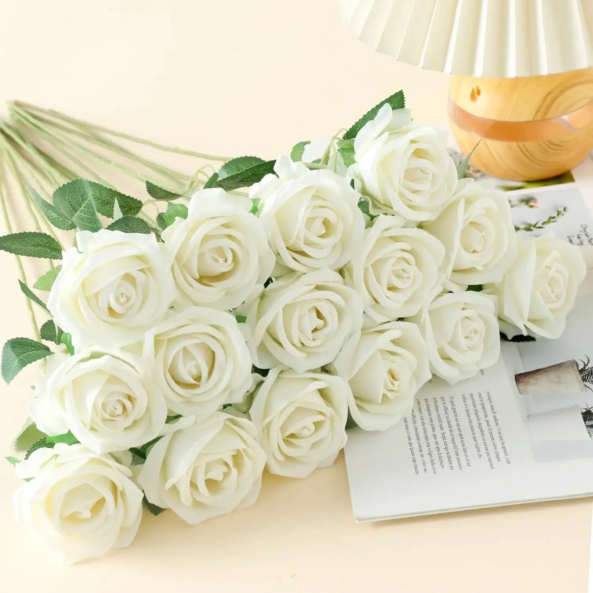 A bouquet of white artificial roses with green leaves displayed on a light background.