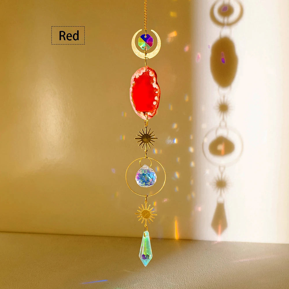 A hanging crystal decor featuring a red agate stone, a clear blue crystal, and a gold sun motif.