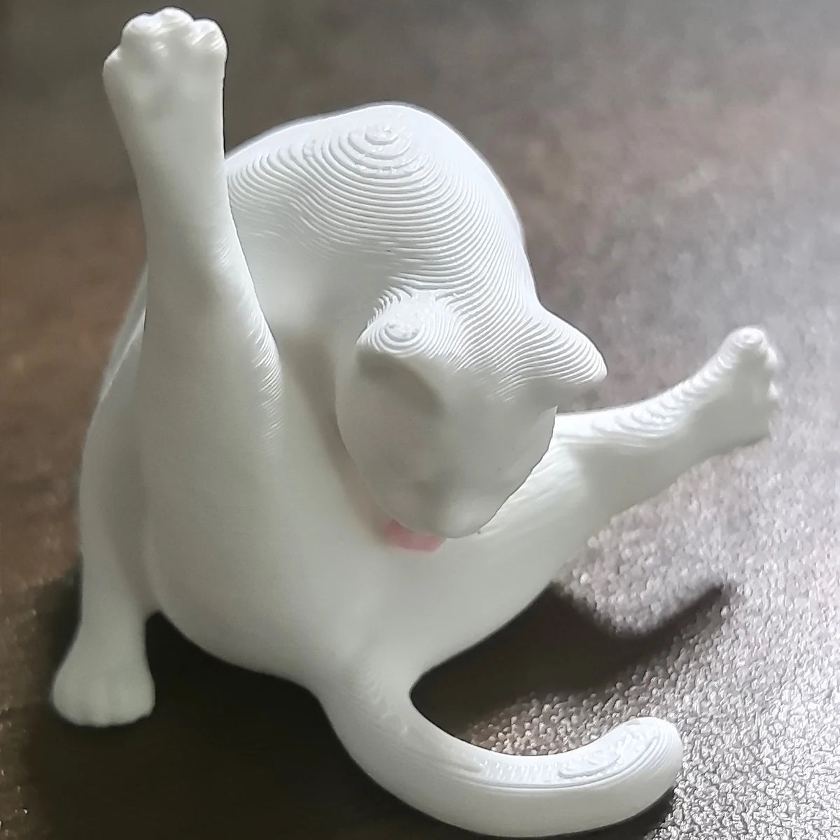 Figura de gato impresa en 3D blanca con lengua rosa asomando, vista de perfil.