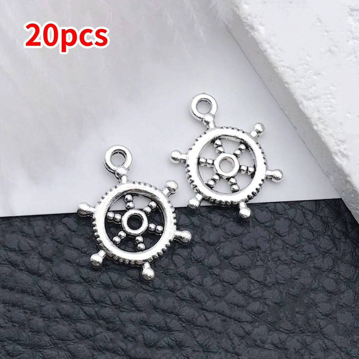 A pair of silver vintage ship anchor charms for jewelry making displayed on a dark surface.
