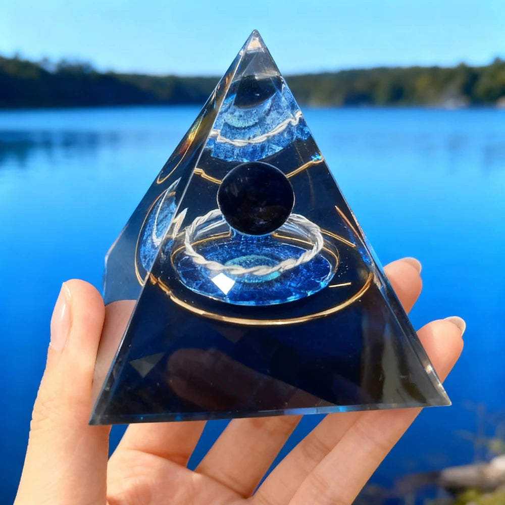 Hand holding a dark blue resin pyramid with an internal copper coil and natural obsidian