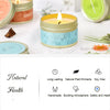 A yellow candle in a light blue tin sits on a white surface next to other candles and natural ingredients.