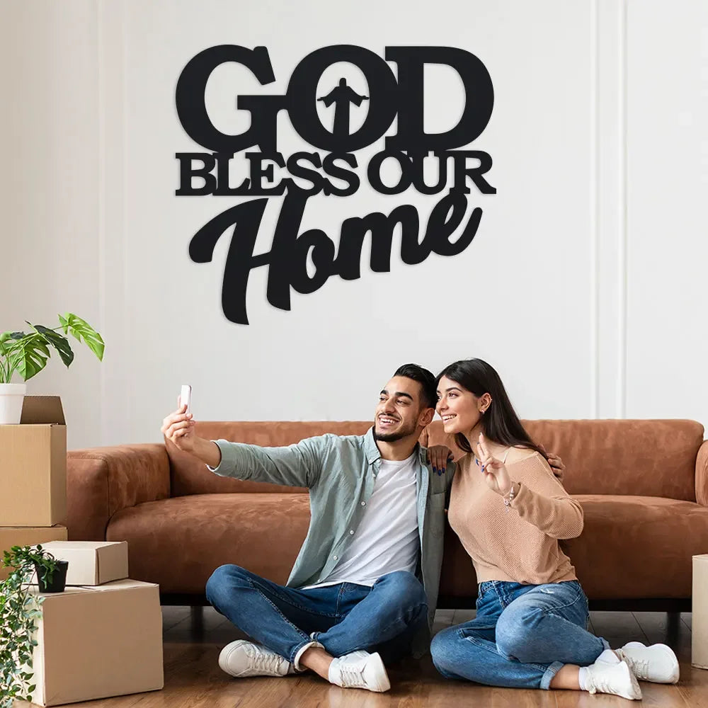 Un couple souriant posant avec une œuvre d'art murale indiquant 'God Bless Our Home'