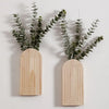 Jarrón de pared arqueado de madera con un ramito de follaje verde sobre fondo blanco.