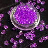 A clear glass bowl filled with purple crystal ice cubes scattered on a dark surface.