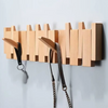 A wooden wall coat rack featuring eight vertical hooks shaped like piano keys, mounted on a light gray wall.
