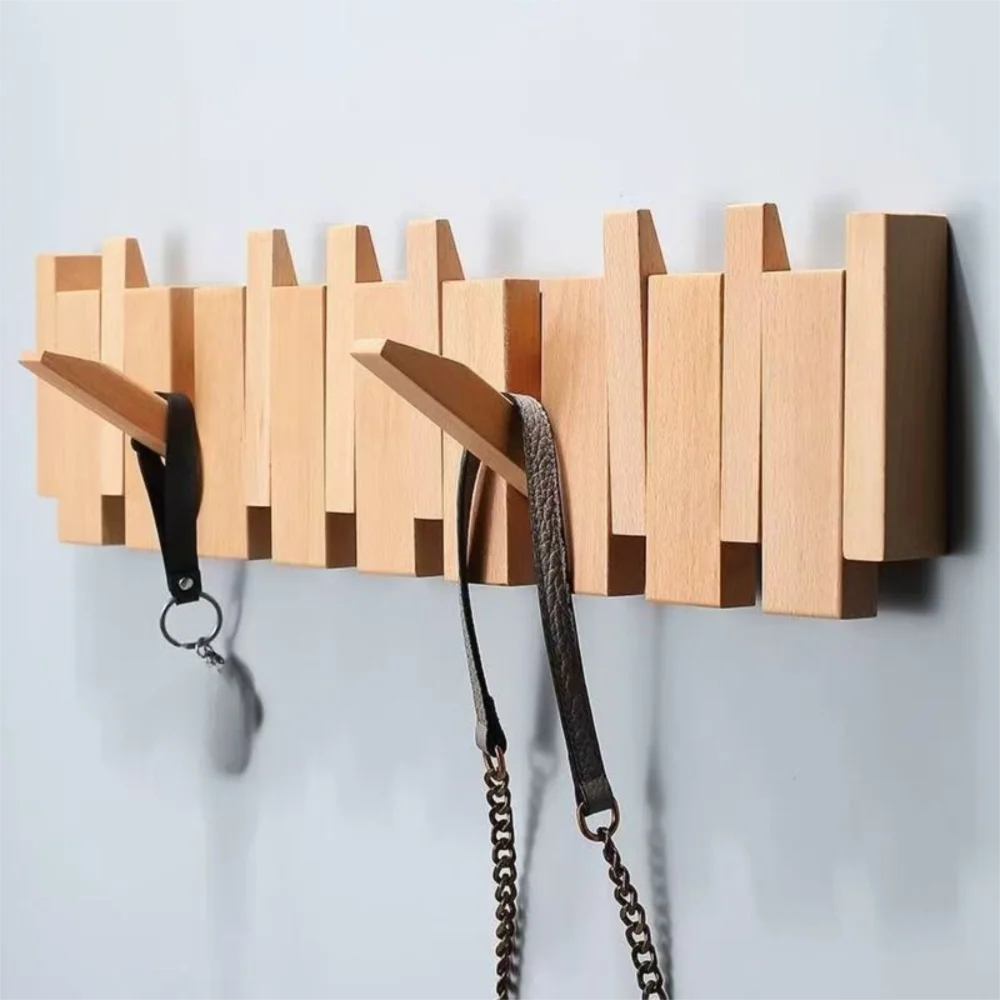 A wooden wall coat rack featuring eight vertical hooks shaped like piano keys, mounted on a light gray wall.