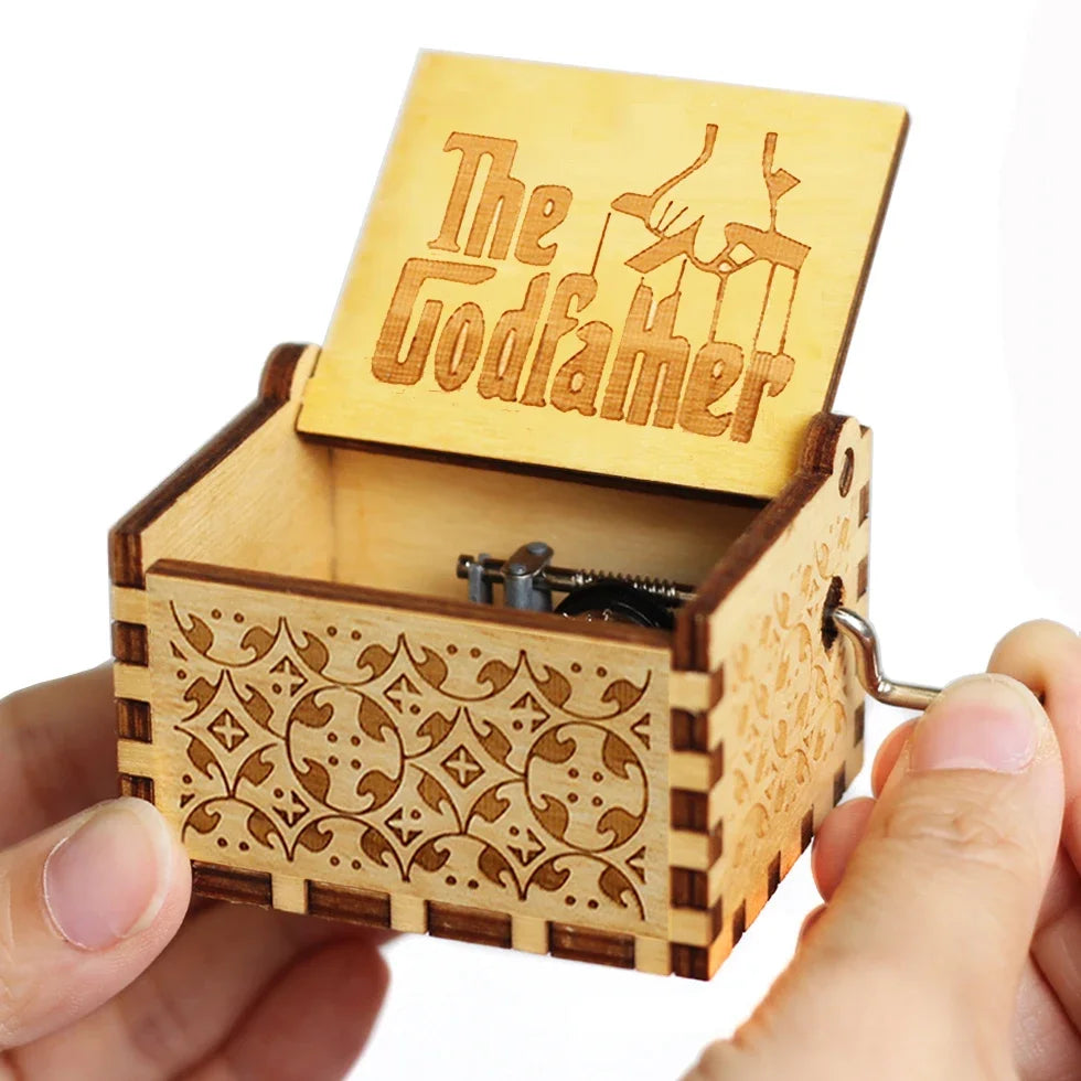 A carved wooden music box with a lid featuring the name The Godfather is held in a hand.