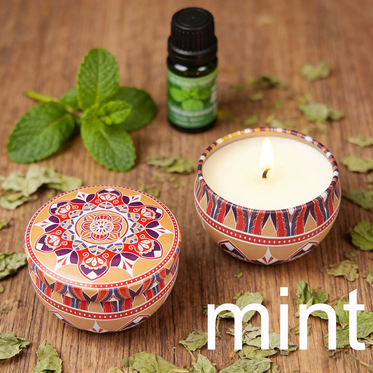 A jar of mint essential oil next to a terracotta candle holder and loose mint leaves on a wooden surface.