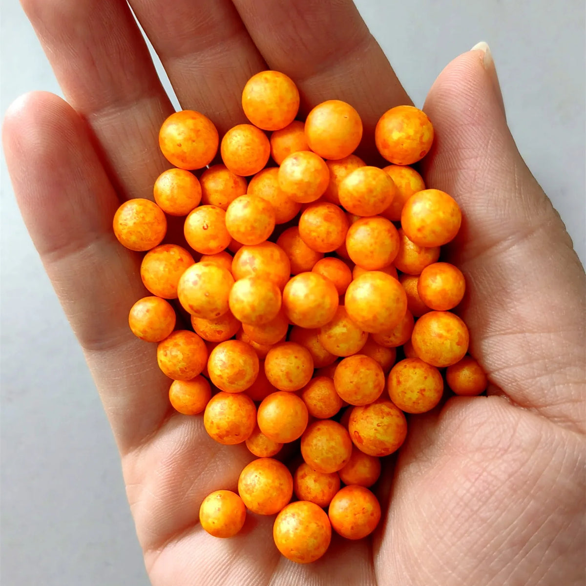 A hand holds a pile of small, round, orange foam beads for crafting and decoration.