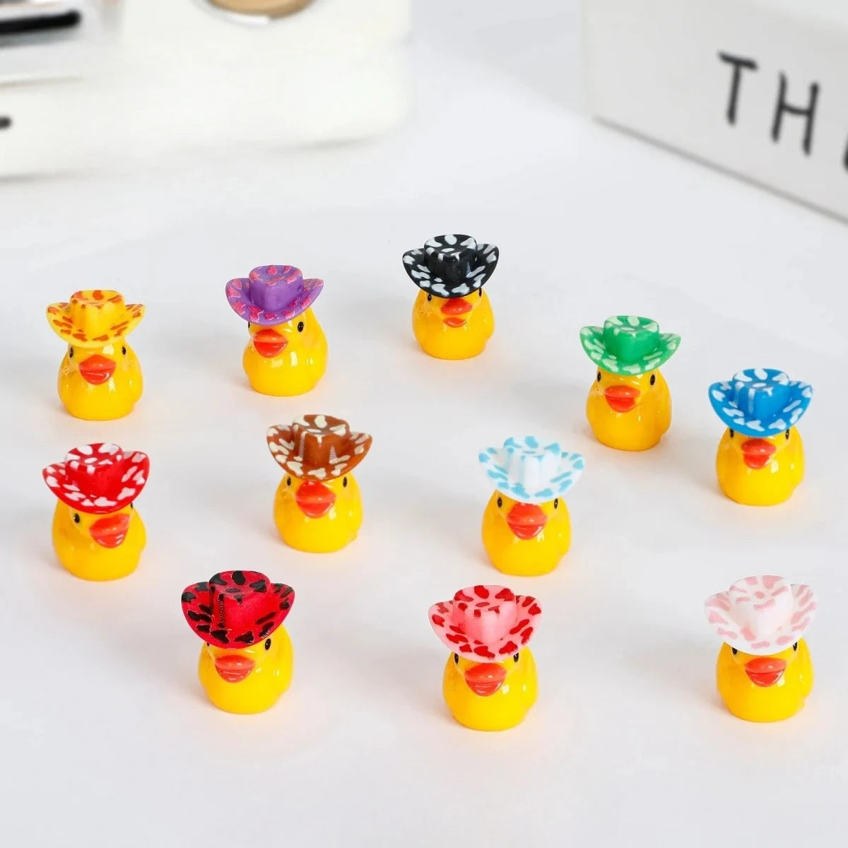 A collection of glow-in-the-dark resin duck figurines with colorful hats, including yellow, purple, black, green, and blue.