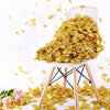 A white ceramic chair holds a pile of gold silk rose petals scattered on a white surface.