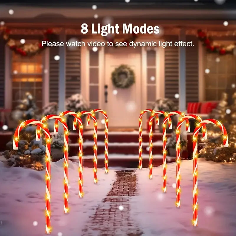 A row of glowing red and white candy cane lights lines a snowy pathway in front of a house.