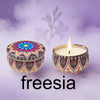 A decorative soy wax candle in a patterned tin set against a soft purple background.