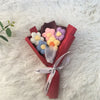 A bouquet of handcrafted crochet sunflowers in pastel colors, wrapped in red paper and tied with a white ribbon, resting on a