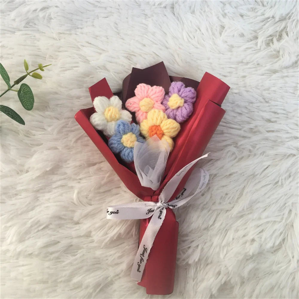 A bouquet of handcrafted crochet sunflowers in pastel colors, wrapped in red paper and tied with a white ribbon, resting on a