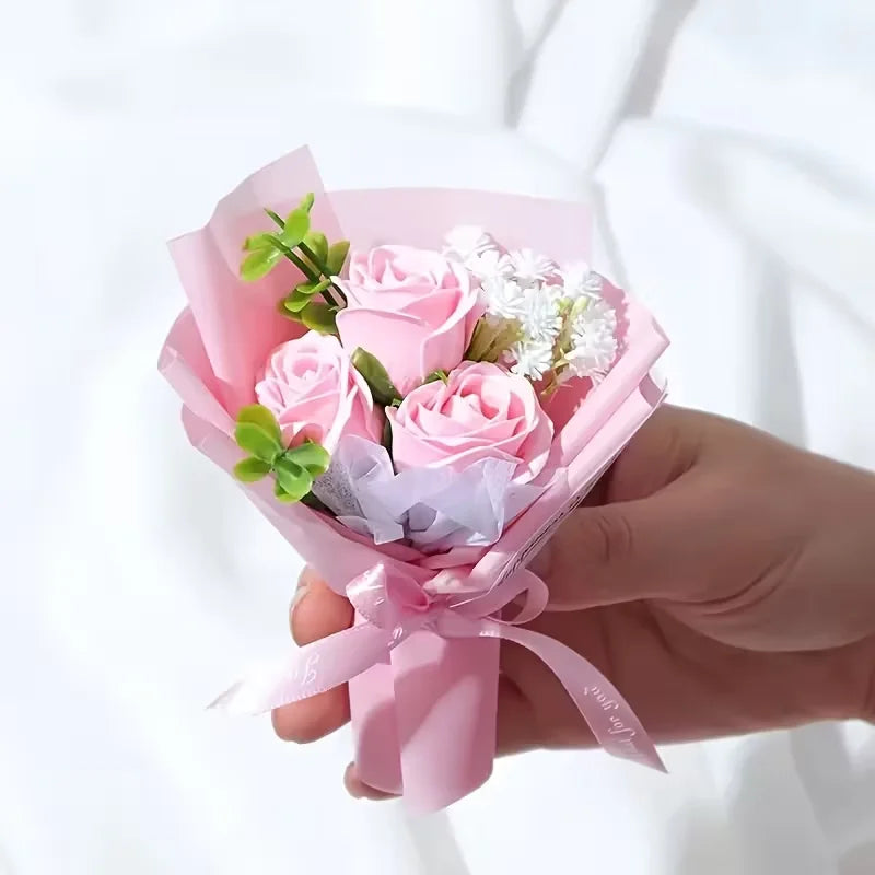 Une main tient un bouquet de mini roses artificielles roses emballées dans du papier rose transparent.