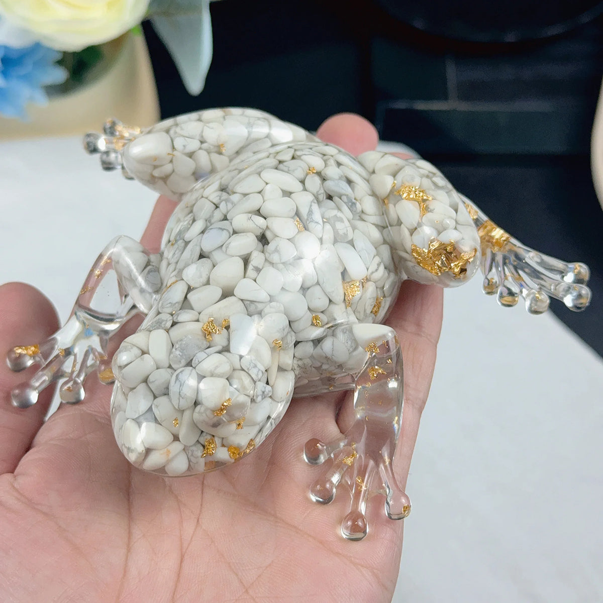 A clear resin crystal craft decoration shaped like a frog with white and gold marbled patterns is held in a hand.