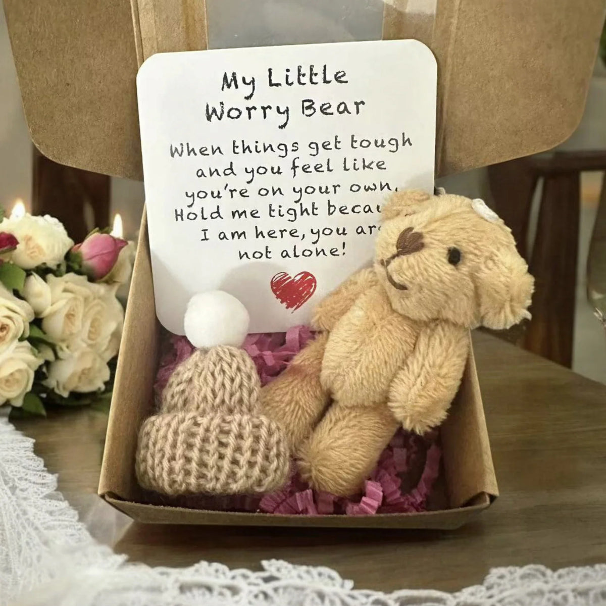 A handmade teddy bear worry plush with an encouraging card resting in a cardboard box lined with purple filler.