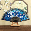 A blue and white floral Spanish style folding lace trim handheld fan displayed against a light background.