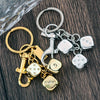 A set of golden dice keychains with lucky charm designs and silver split rings on a dark wooden surface.