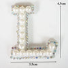 A white alphabet letter T made of pearl and rhinestone patches on a clear background.