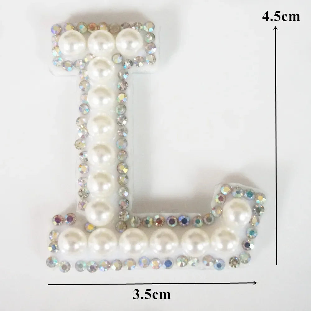 A white alphabet letter T made of pearl and rhinestone patches on a clear background.