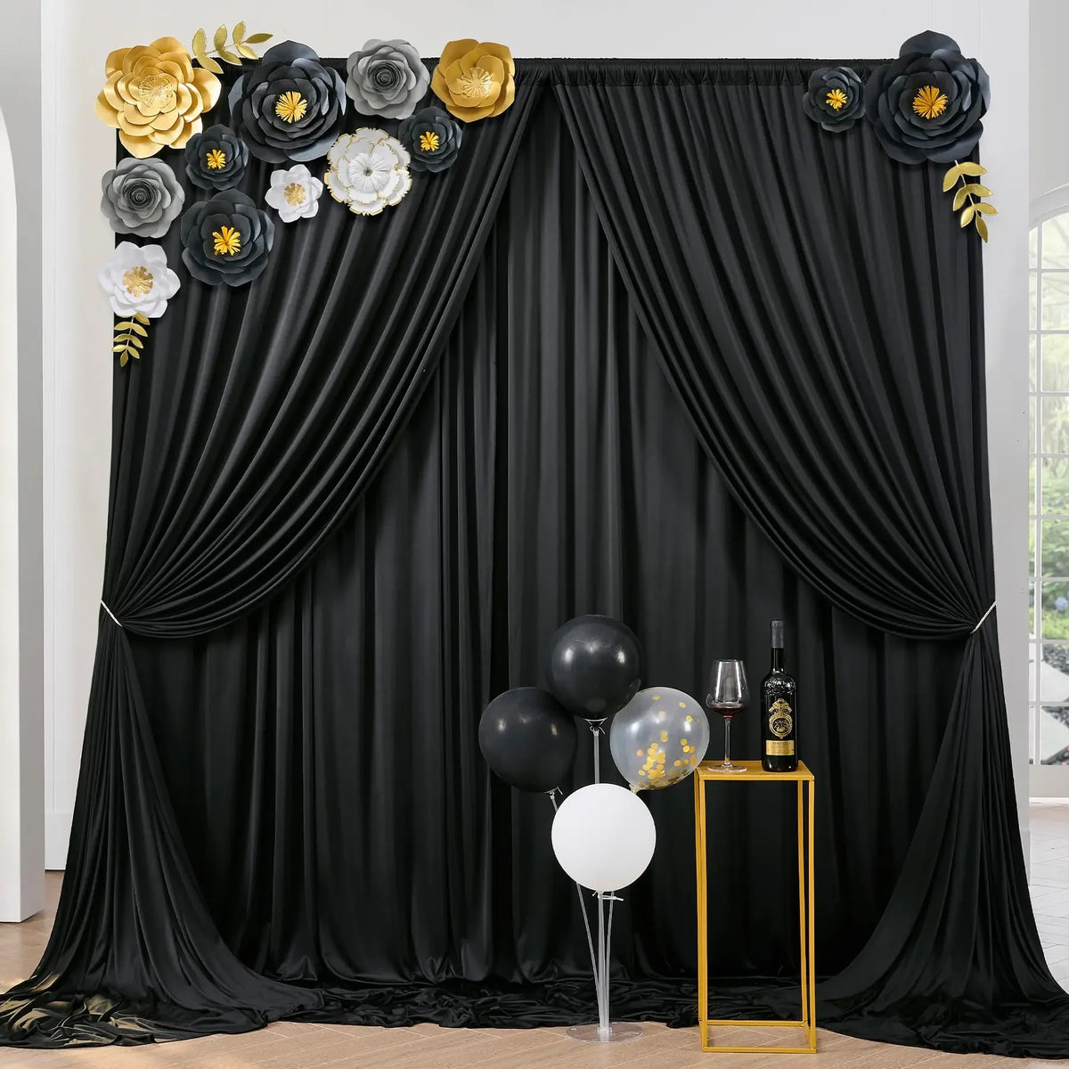 A black draped curtain backdrop decorated with gold and gray floral accents for parties and photography.
