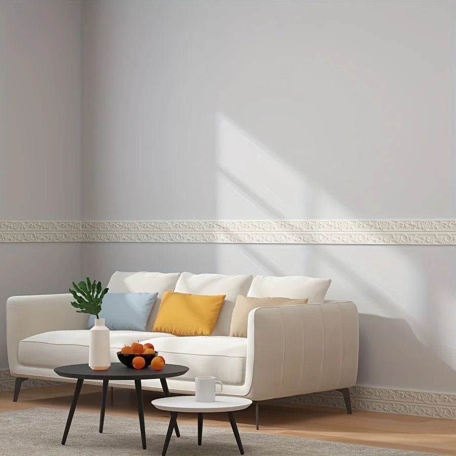 A white upholstered sofa with yellow and blue cushions is placed against a light gray wall with decorative molding.