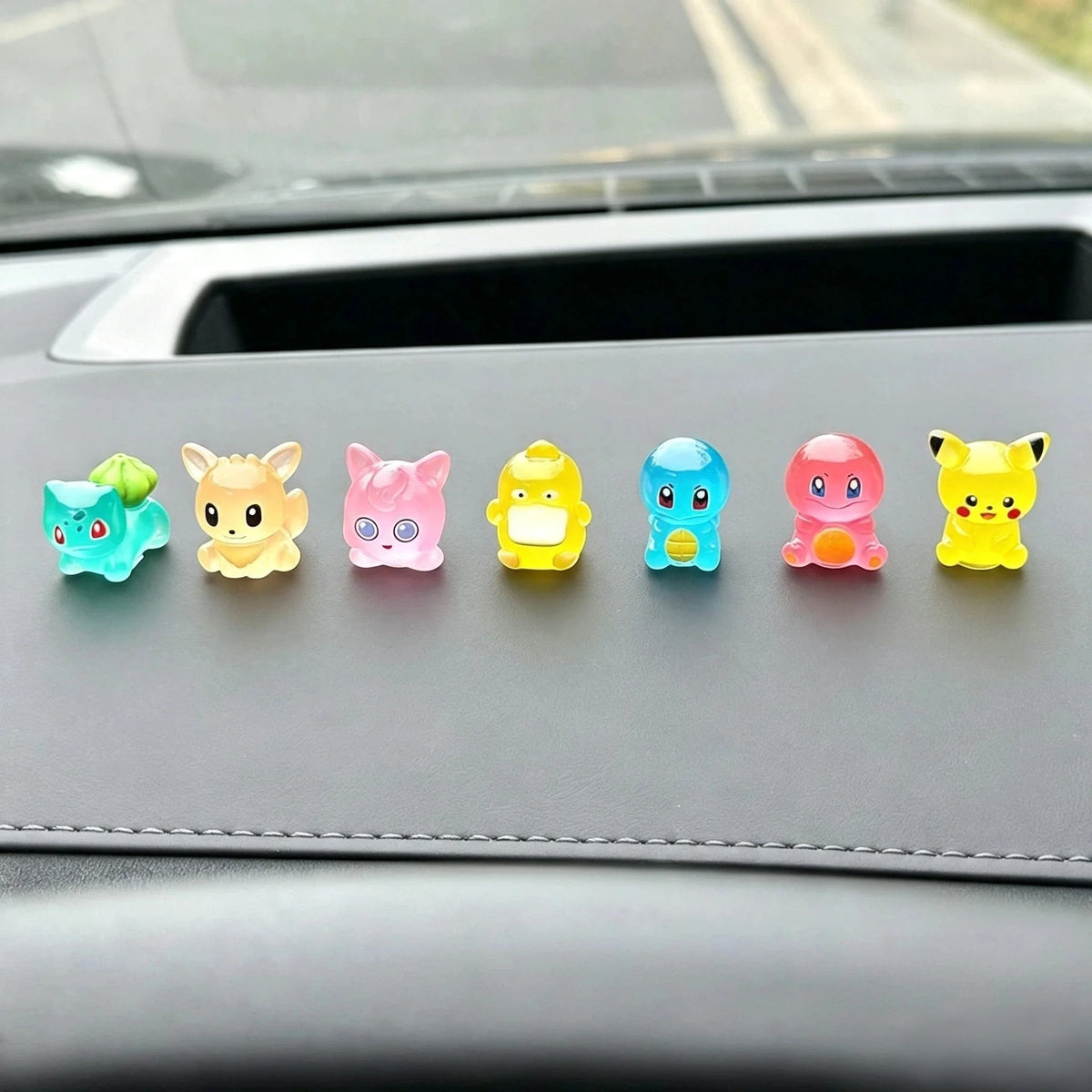 A set of six colorful kawaii anime fantasy creature mini figurines lined up on a car dashboard.
