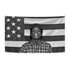 A person wearing a patterned shirt is centered on a black and white American flag tapestry.
