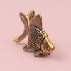 A small, detailed retro brass goldfish statue with textured scales and fins, resting on a pink surface.