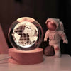 A 3D crystal ball night light with a glowing Earth sphere sits on a wooden base.