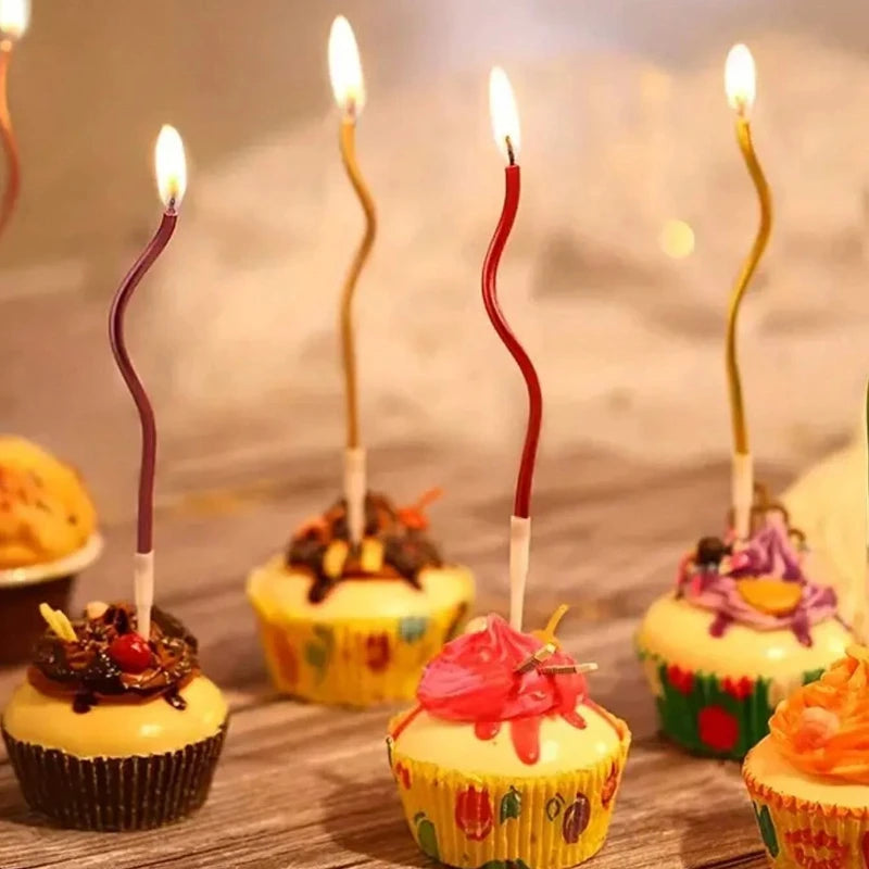 A set of curved decorative birthday candles placed in yellow cupcake liners on a wooden surface.