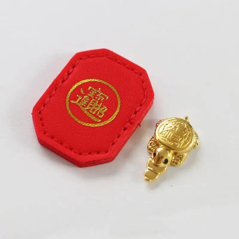 A red felt tag with a gold circular emblem and a small golden tortoise figurine.